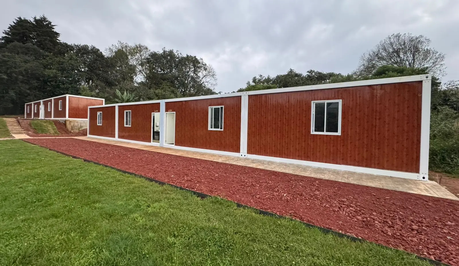 Hilera de cabañas modulares rojas con ventanas blancas junto a un camino